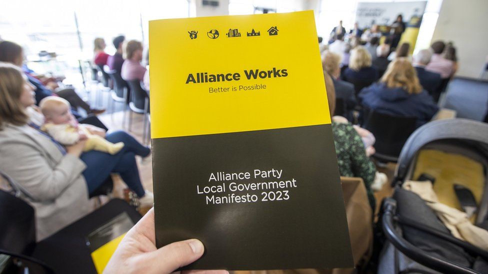 A man holds a copy of The Alliance Party's 2023 council elections manifesto