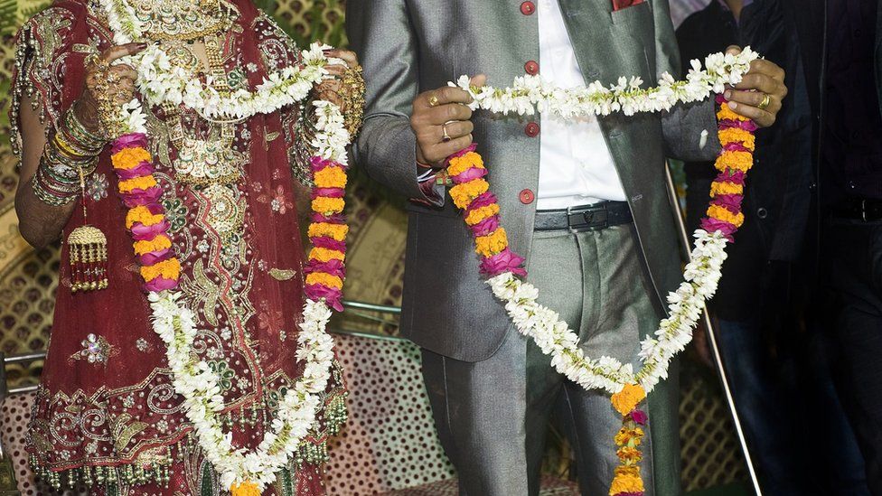 Photo showing bride and groom holding flower garlands