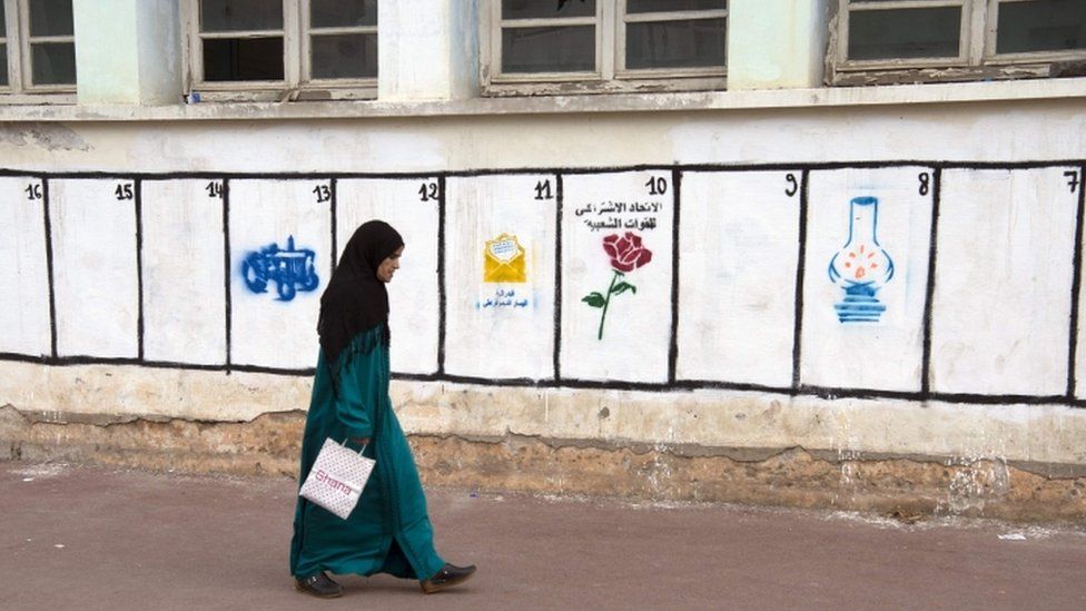 Woman walks past party symbols on a wall in Rabat, 7 October 2016