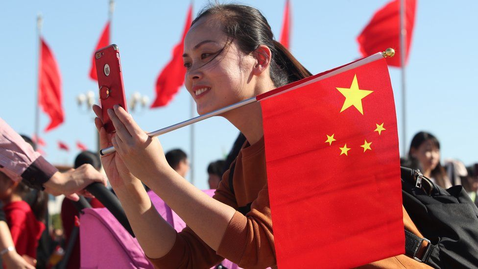 A tourist holding a Chinese national flag takes pictures at the Tiananmen Square during the Chinese National Day holiday on October 3, 2018 in Beijing, China.