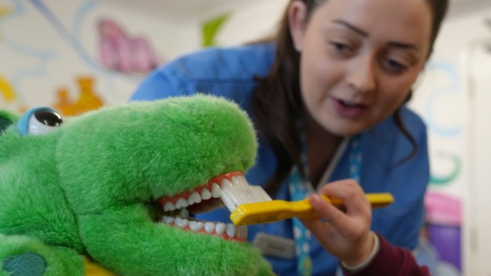 dental nurse and child brushing a dinosaur's teeth