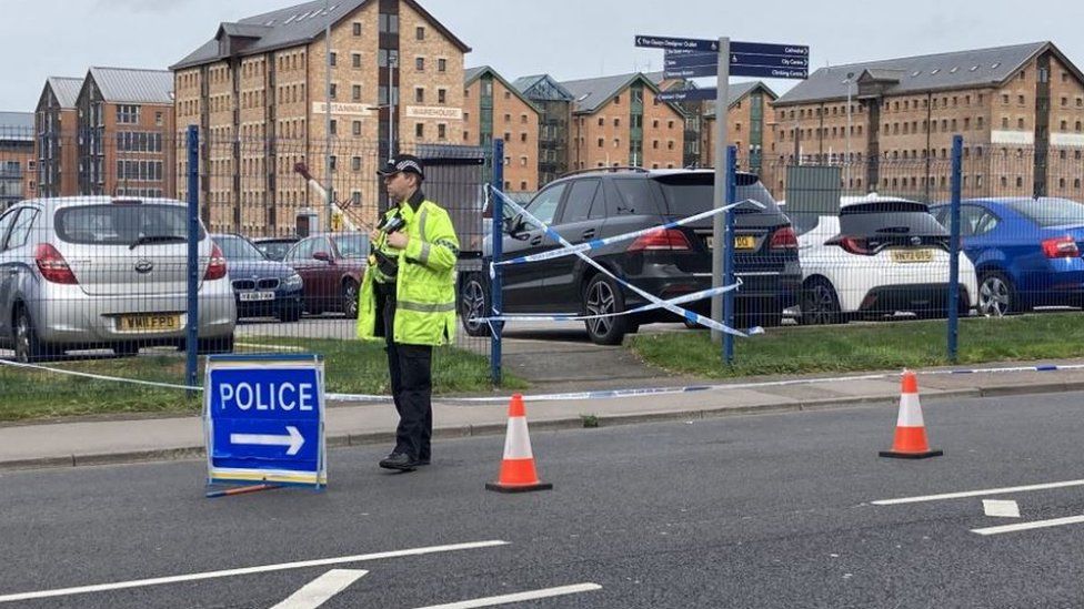 A police officer stood behind cones and a police sign on Southgate Street with Gloucester Docks in the background