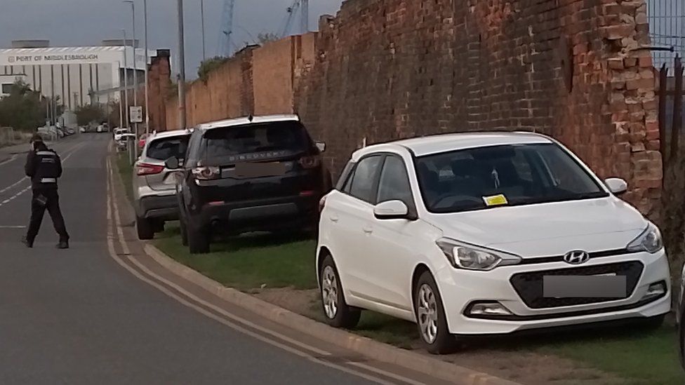 Illegally parked cars on grass verge with tickets