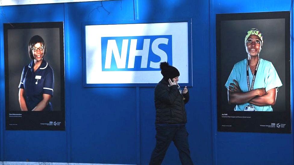 An NHS sign on a wall with pictures of two NHS workers