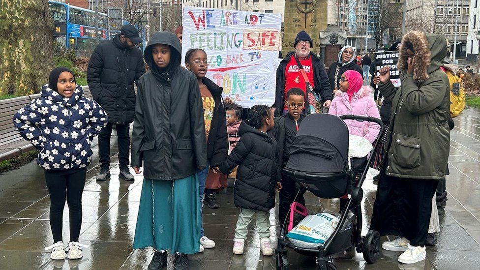 Barton House residents - adults and children, standing together, holding signs