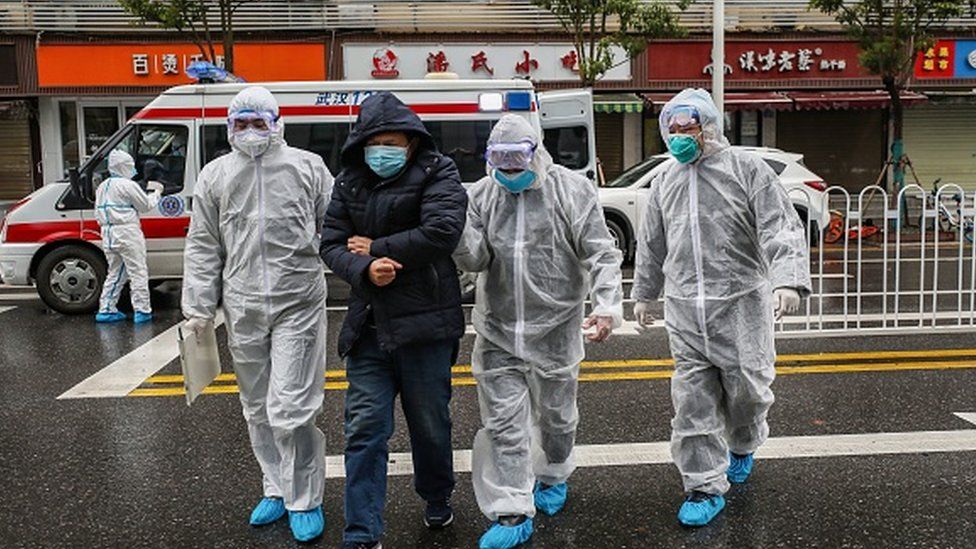 Medical staff members wearing protective clothing accompany a patient as they walk into a hospital in Wuhan