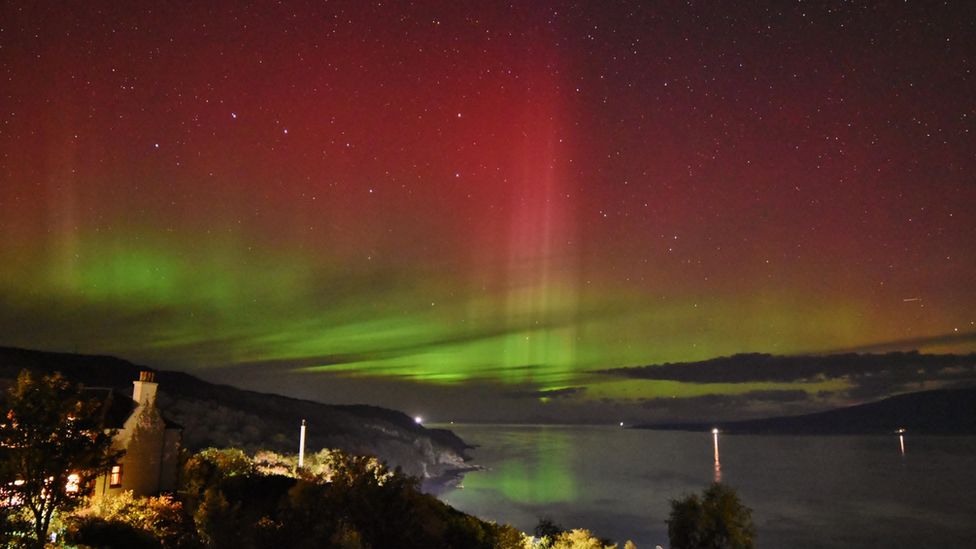 Looking over Port Askaig with vivid greens close to the horizon in the night sky with lots of red higher in sky.