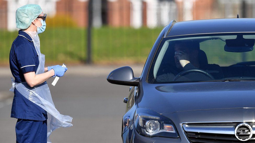 A medical staff member wearing PPE of gloves, eye protection, a face mask and an apron, prepares to test an NHS worker for the novel coronavirus COVID-19, at a drive-in facility run by Wolverhampton NHS Clinical Commissioning Group, set up in a car park in Wolverhampton, central England