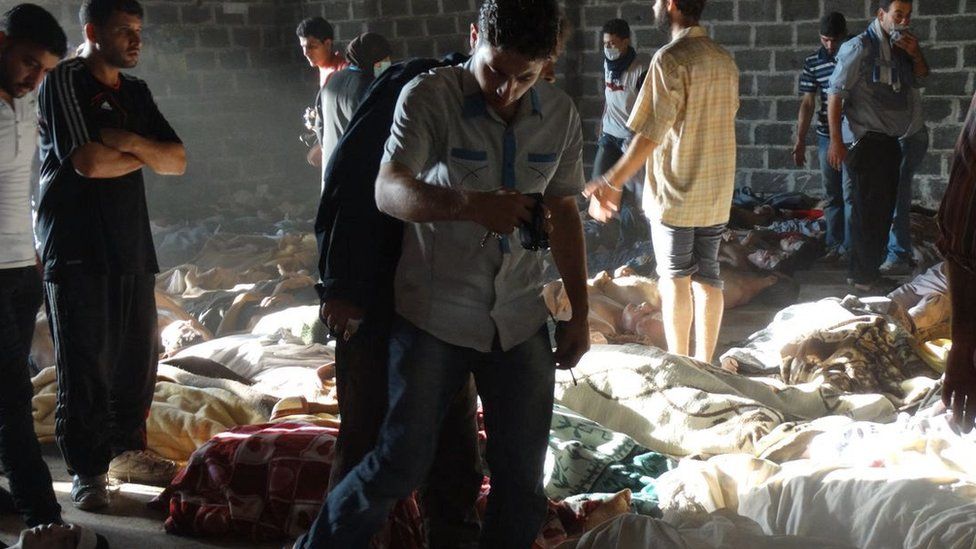 Люди смотрят на тела людей, погибших в результате атаки нервно-паралитического агента зарина в контролируемом повстанцами районе Гута в Дамаске 21 августа 2013 г.