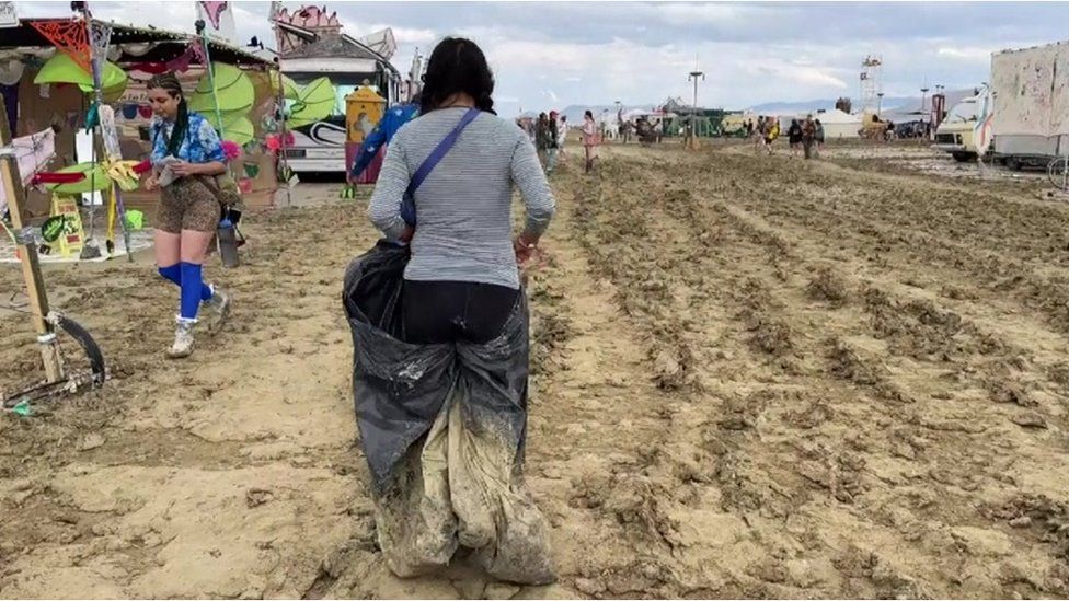 Женщина идет по грязи с мешком для мусора на фестивале Burning Man в Неваде
