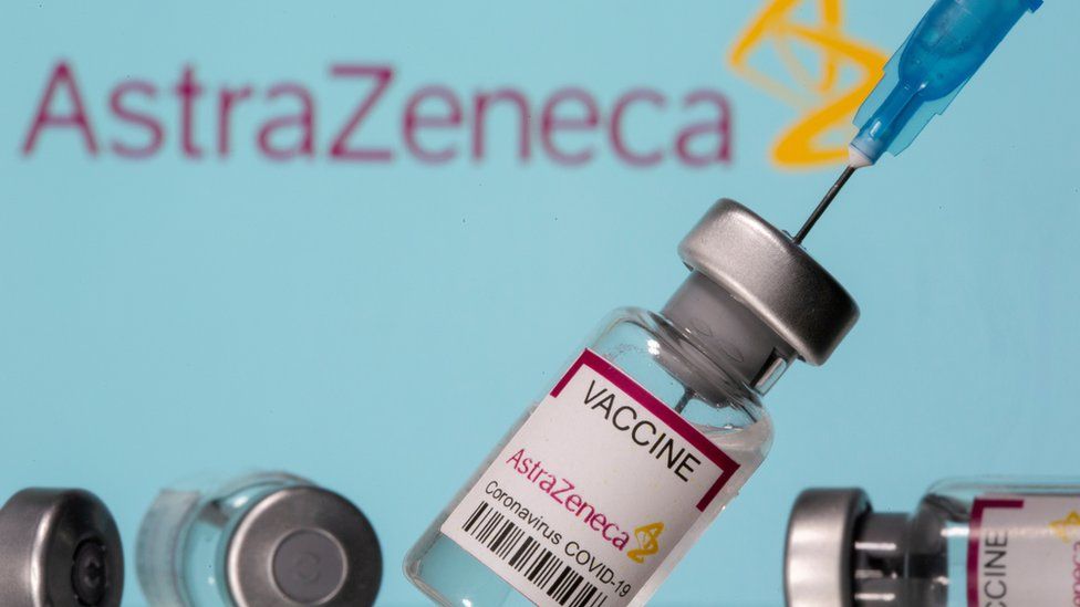 Флаконы с надписью «Astra Zeneca COVID-19 Coronavirus Vaccine» и шприц видны перед отображаемым логотипом AstraZeneca на этой фотографии, сделанной 14 марта 2021 года.