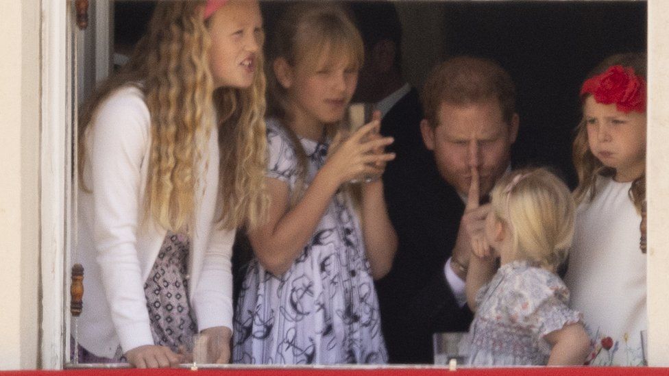Prince Harry puts his finger to his lips with Savannah Phillips and Mia Tindall in the Major General's office overlooking The Trooping of the Colour