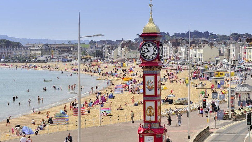 a shot of weymouth beach with a red clock in the foreground