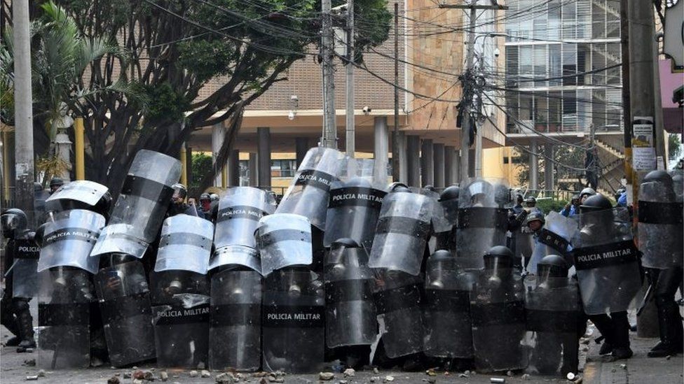 Honduran riot police take cover during clashes with students of the National Autonomous University of Honduras (UNAH) and elementary school teachers who protest against the approval of education and healthcare bills in the Honduran Congress in Tegucigalpa on April 29, 2019