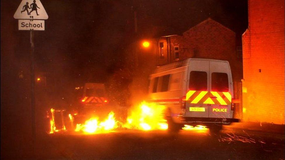 Police vans drive through flames during the 2001 riots