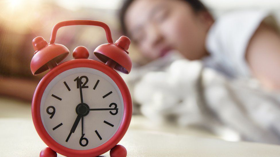 A woman asleep with an alarm clock