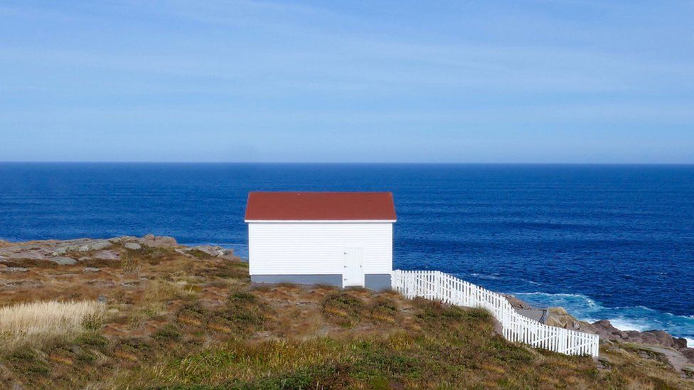 A small house, and white picket fence, overlooks the Atlantic on the wild east coast of Newfoundland