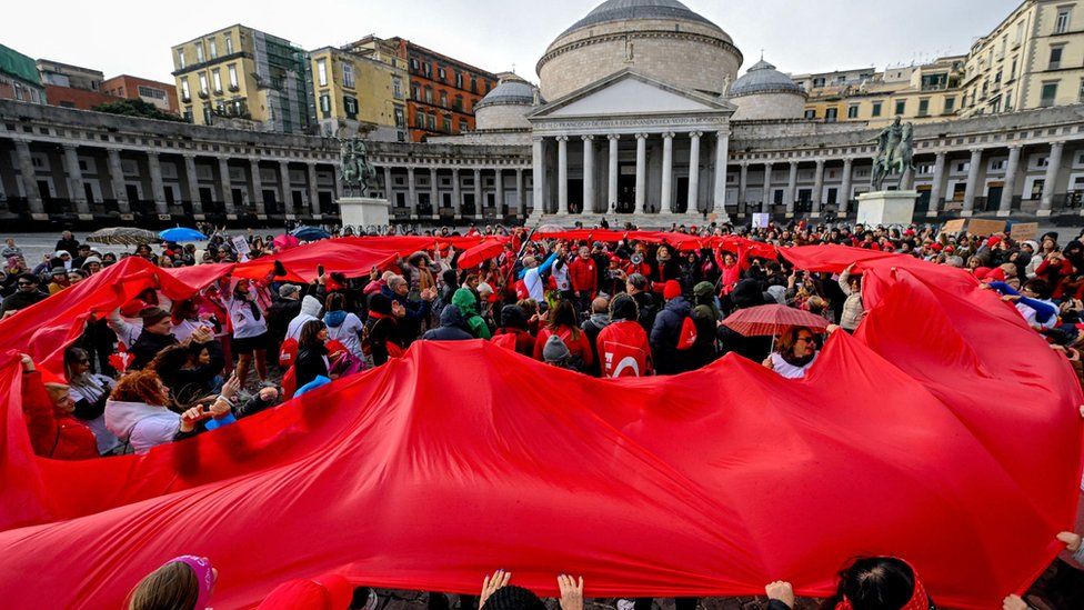 A large crowd of protesters in Naples holding a large red cloth