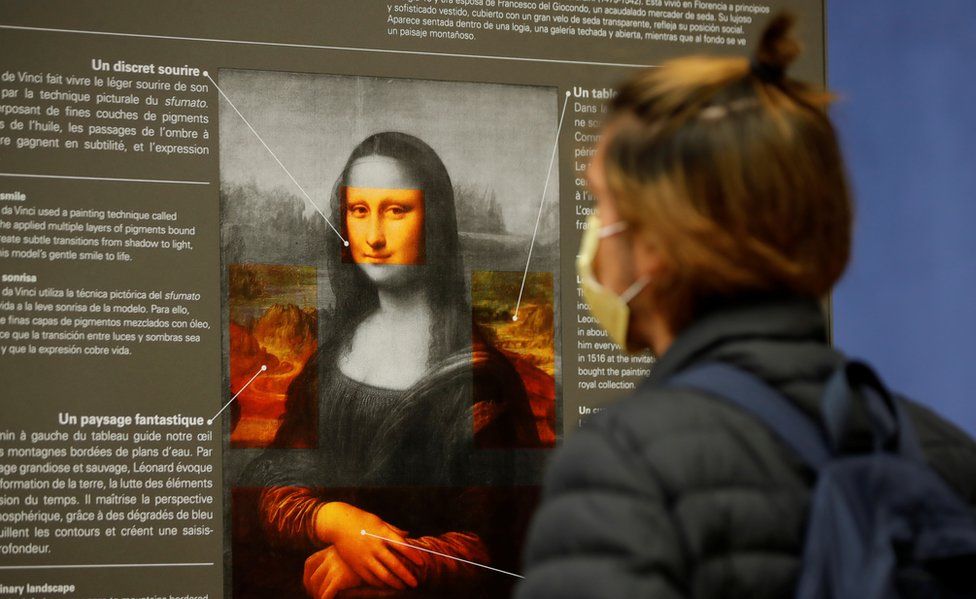Посетитель в защитной маске смотрит на плакат с пояснениями к картине Леонардо да Винчи «Мона Лиза» (La Joconde) в Лувре в Париже 19 мая
