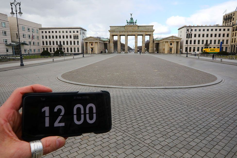 A digital clock on a smartphone is pictured in front of Brandenburg gate, Berlin, Germany.