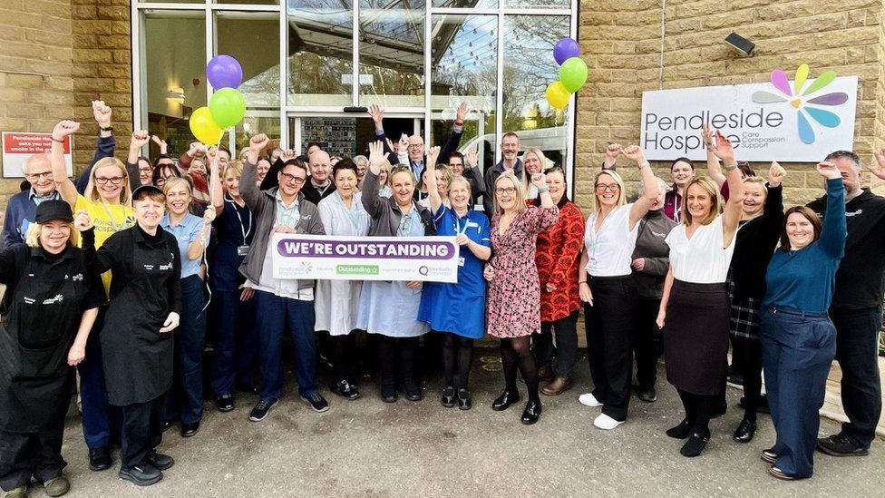 Pendleside Hospice holding a banner saying outstanding to celebrate its CQC rating