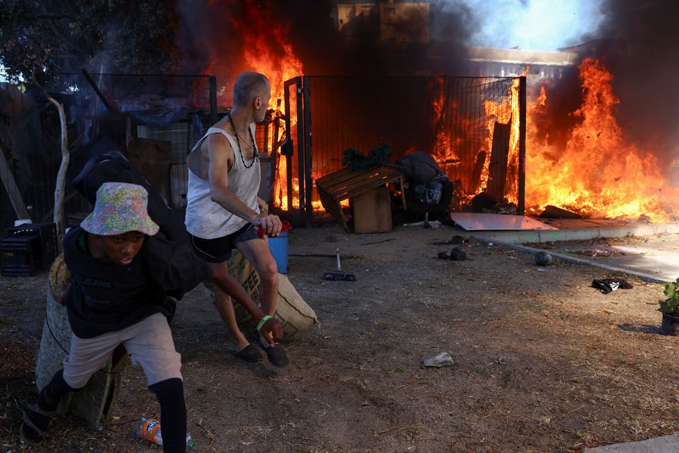 Occupants remove their belongings from makeshift shelters which are on fire near the Green Point tennis courts in Cape Town, South Africa, February 22, 2024.