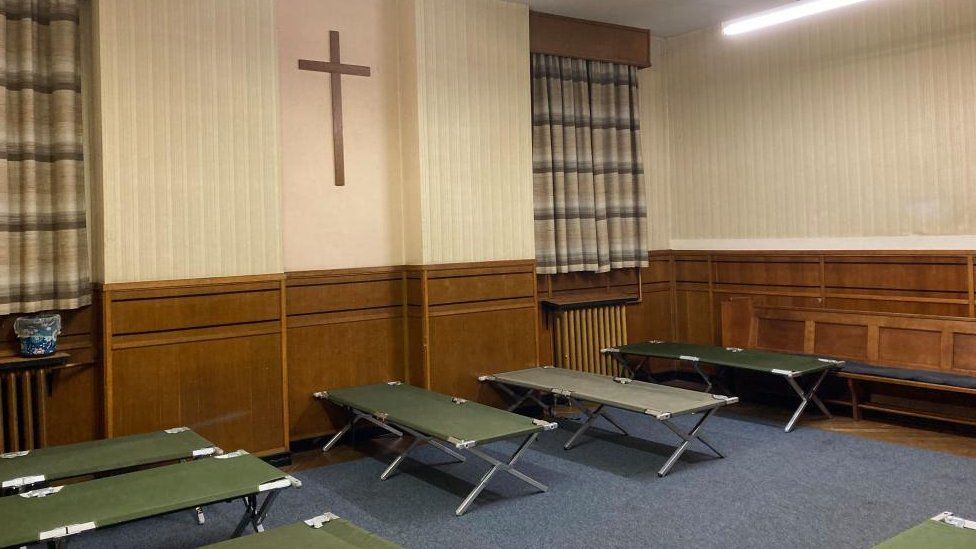 Room at church with a cross on the wall and green campbeds on the floor