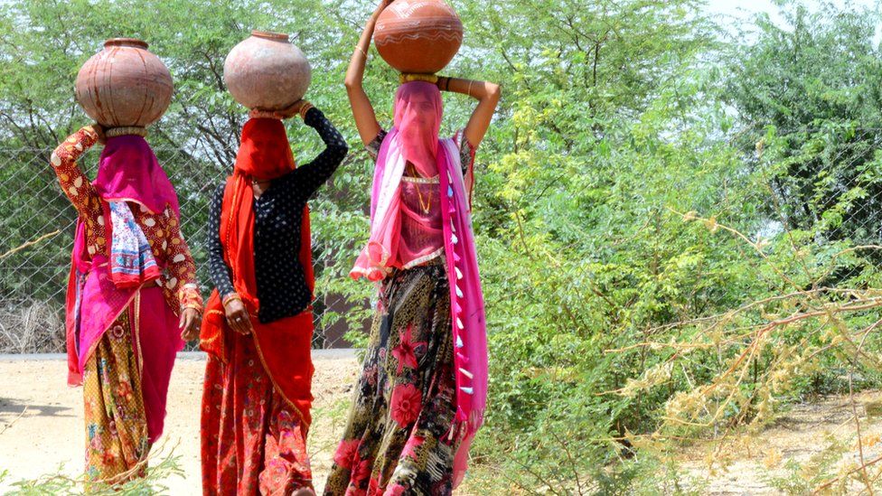 Village women carry clay pots filled with drinking water to their homes from a public tap during a hot summer day, on the outskirts of Beawar.