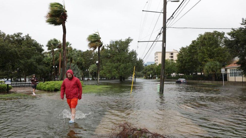 A man in a red jacket walks through a flooded street in Orlando, Florida.