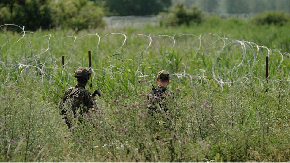 Polish border guards patrol alongside a barbed wire fence
