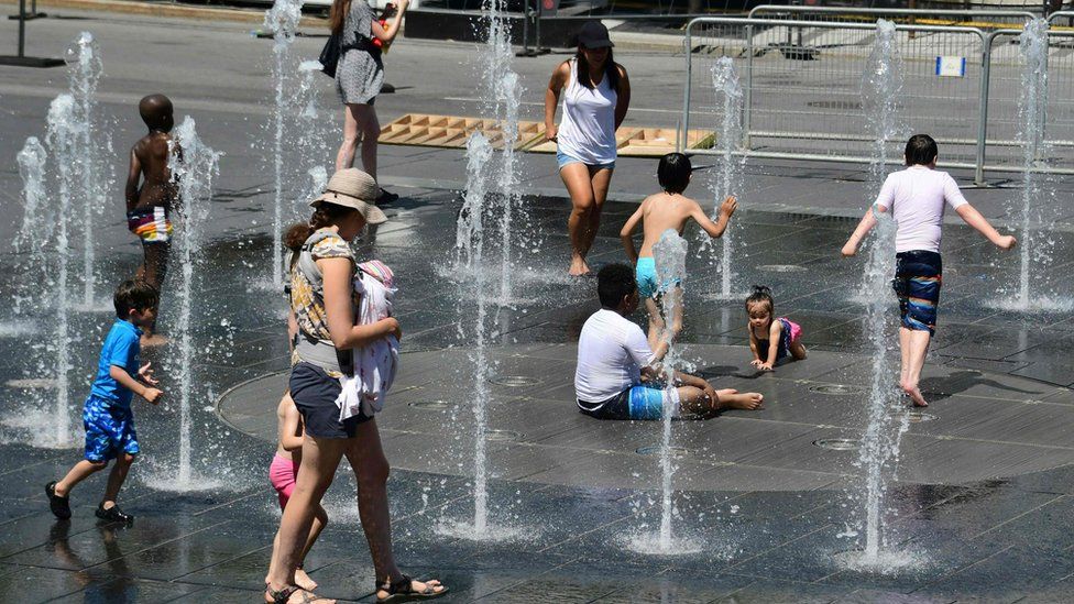 A group of people pictured trying to stay cool in a fountain