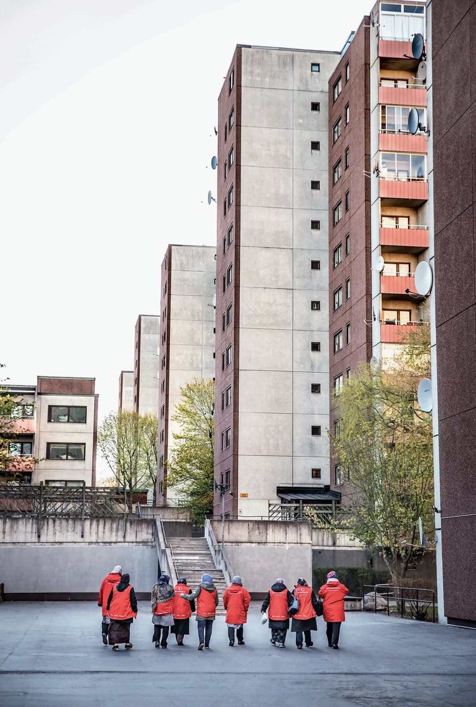 A line of women in red coats make their way through a housing development.