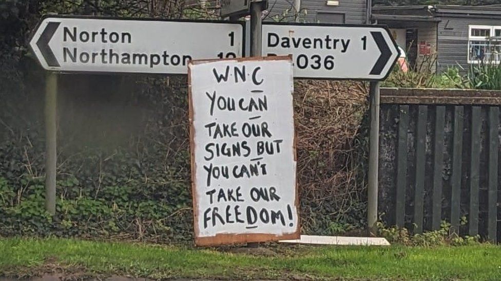Hand-painted sign attached to road sign saying "WNC You can take our signs but you can't take our freedom"