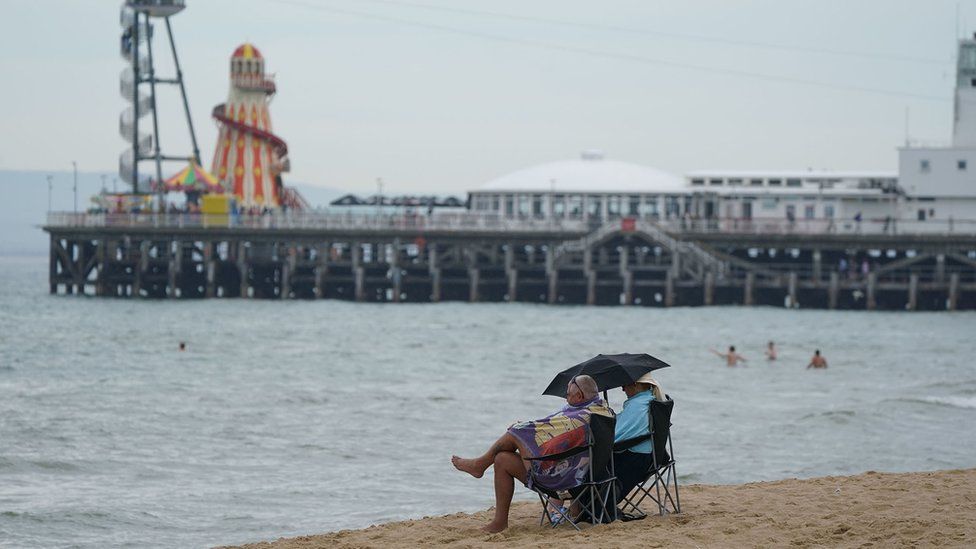 A couple shelter beneath an umbrella at Bournemouth beach in Dorset. The UK has recorded its third successive warmest day of the year