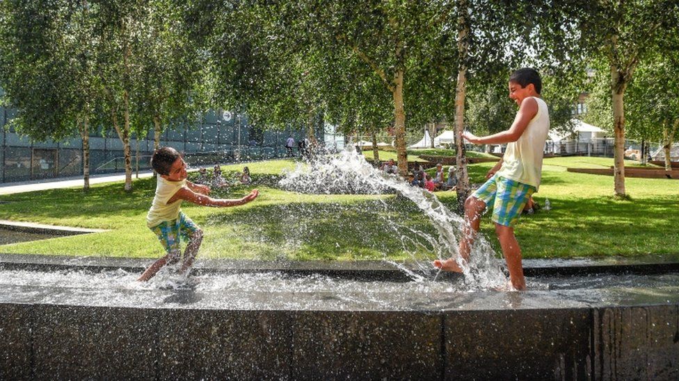 Two boys splash in the water feature beside the National Football Museum in central Manchester