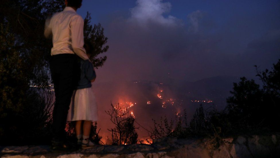 A man and his daughter watch as wildfire burns on a hill near Shoeva, on the outskirts of Jerusalem, 15 August 2021