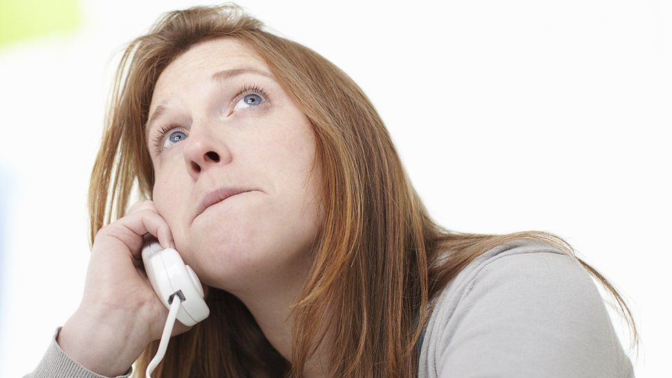 A woman looks to the sky, clearly bored while on hold on the phone pressed to her ear