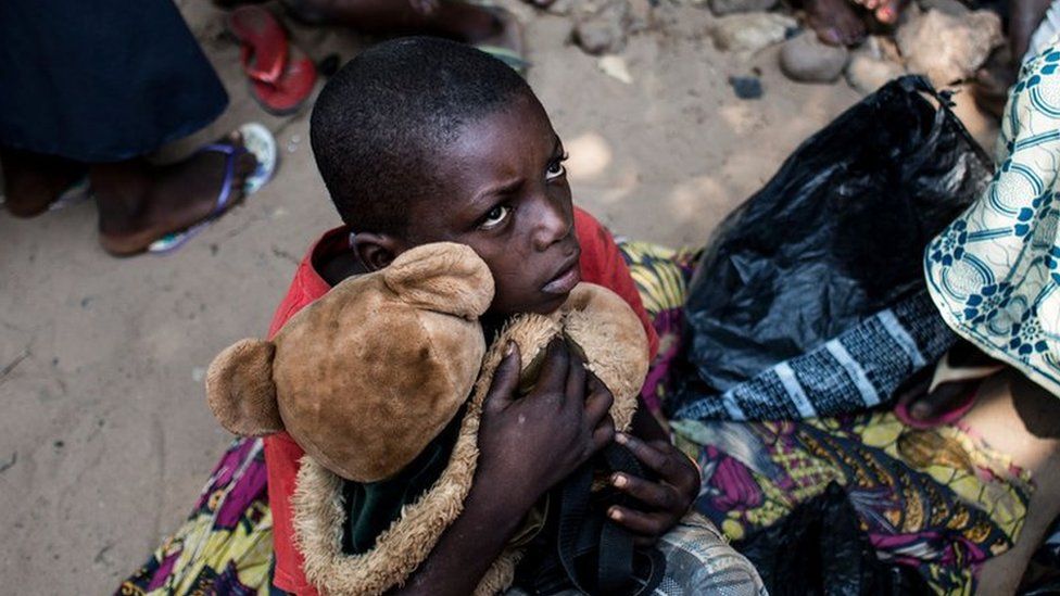A boy holds his teddy bear as he waits with other Internally Displaced Persons (IDP) for a daily food ration at a camp for IDP"s fleeing the conflict in the Kasai Province on June 7, 2017 in Kikwit.