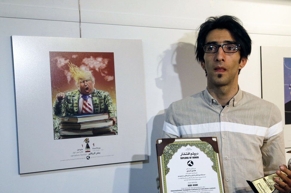 Iranian cartoonist Hadi Asadi poses for a picture with a trophy and an award next to cartoons of US President Donald . Trump, at an exhibition of the Islamic Republic's 2017 International Trumpism cartoon and caricature contest, in the capital Tehran on 3 July 2017.