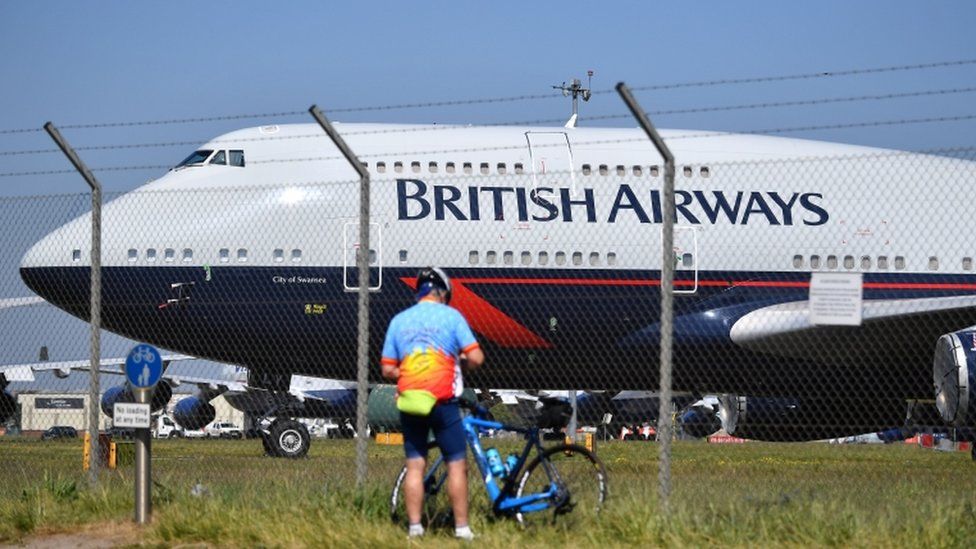 A cyclist standing near a British Airways plane