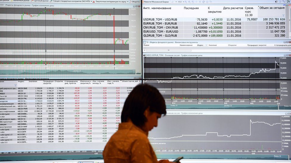 A woman stands in front of a screen showing stock market movements at the office of the Moscow stock exchange, on 11 January 2016