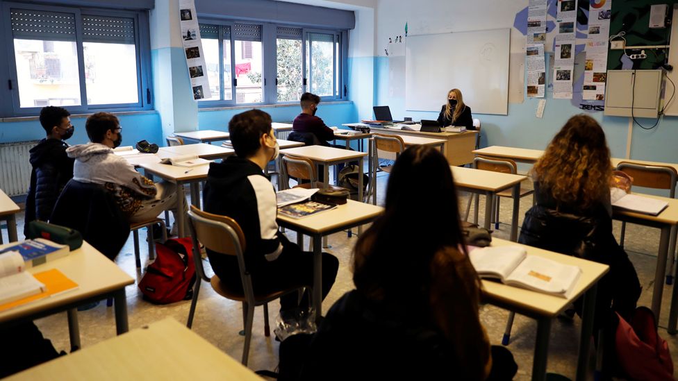 Students and a teacher sit in a classroom in Rome, wearing masks and socially distancing