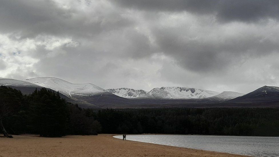 A view of a beach and a lake with snow-topped mountains in the background
