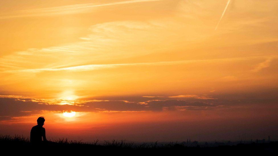 A man sitting at Drachenberg mountain watches the sun rising over Berlin on June 26, 2019