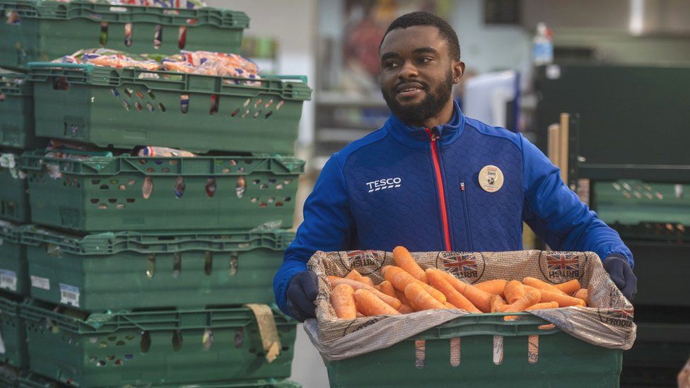Tesco worker moving crate of carrots