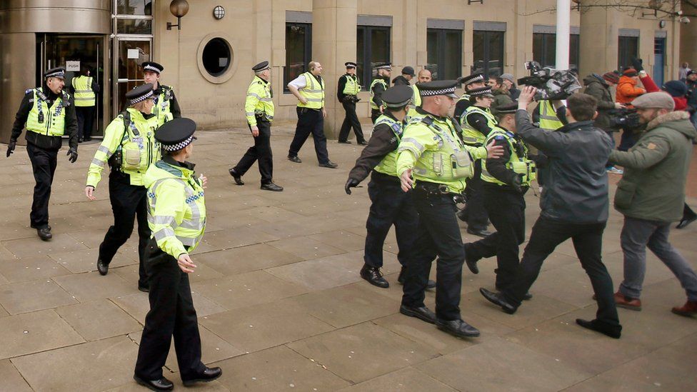 Police officers shepherd the media after the arrival of former England footballer Adam Johnson at Bradford Crown Court