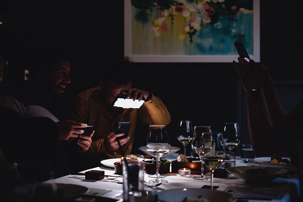 Two men take photos of the their food in a restaurant