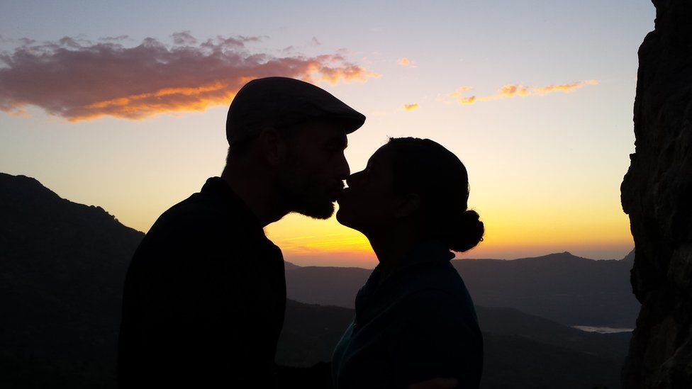 A man and woman kiss each other at sunset