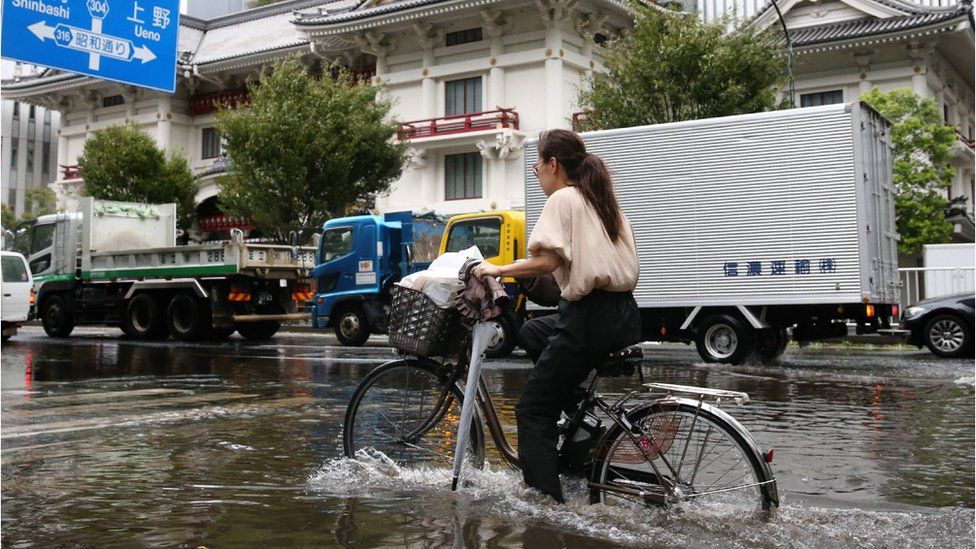A woman cycles through a flooded area in Tokyo
