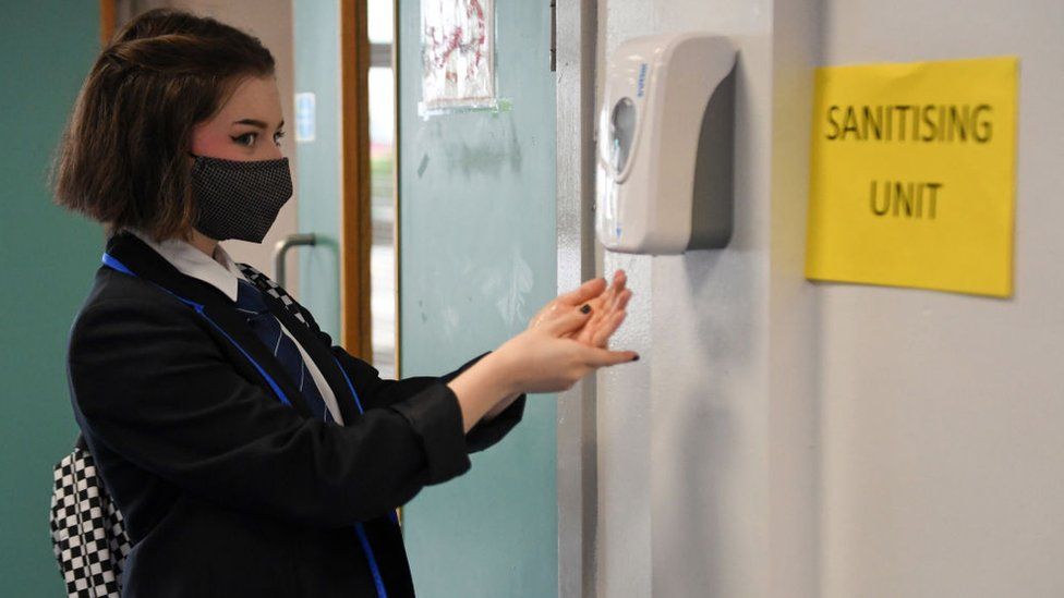 A girl wearing a face mask uses a school hand sanitiser unit